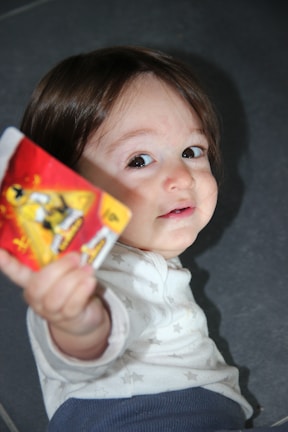 A young child with long brown hair looks up with a curious expression, holding a card with vibrant colors, including red and yellow, depicting a character in a dynamic pose.