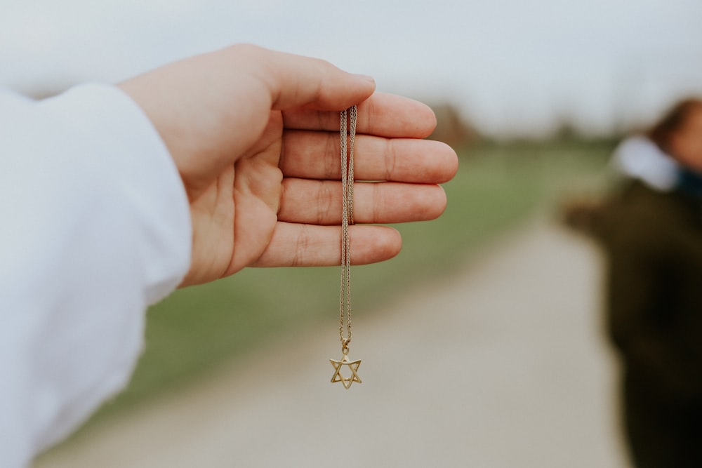 person holding gold cross pendant necklace
