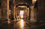 Shadowy interior of a temple room with faint glowing hieroglyphs and Guarani motifs on the walls.