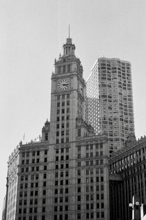 Two prominent high-rise buildings stand side by side, one featuring a clock tower design. The architecture is classic, with intricate details and a sense of historic grandeur. The scene is rendered in black and white, enhancing the timeless feel.