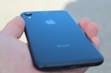 A hand holding a sleek, black smartphone with the Apple logo visible on the back.
