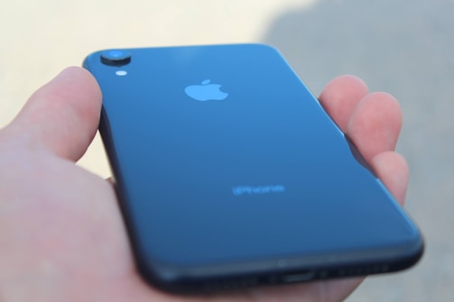 A hand holding a sleek, black smartphone with the Apple logo visible on the back.
