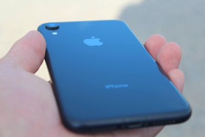 A hand holding a sleek, black smartphone with the Apple logo visible on the back.