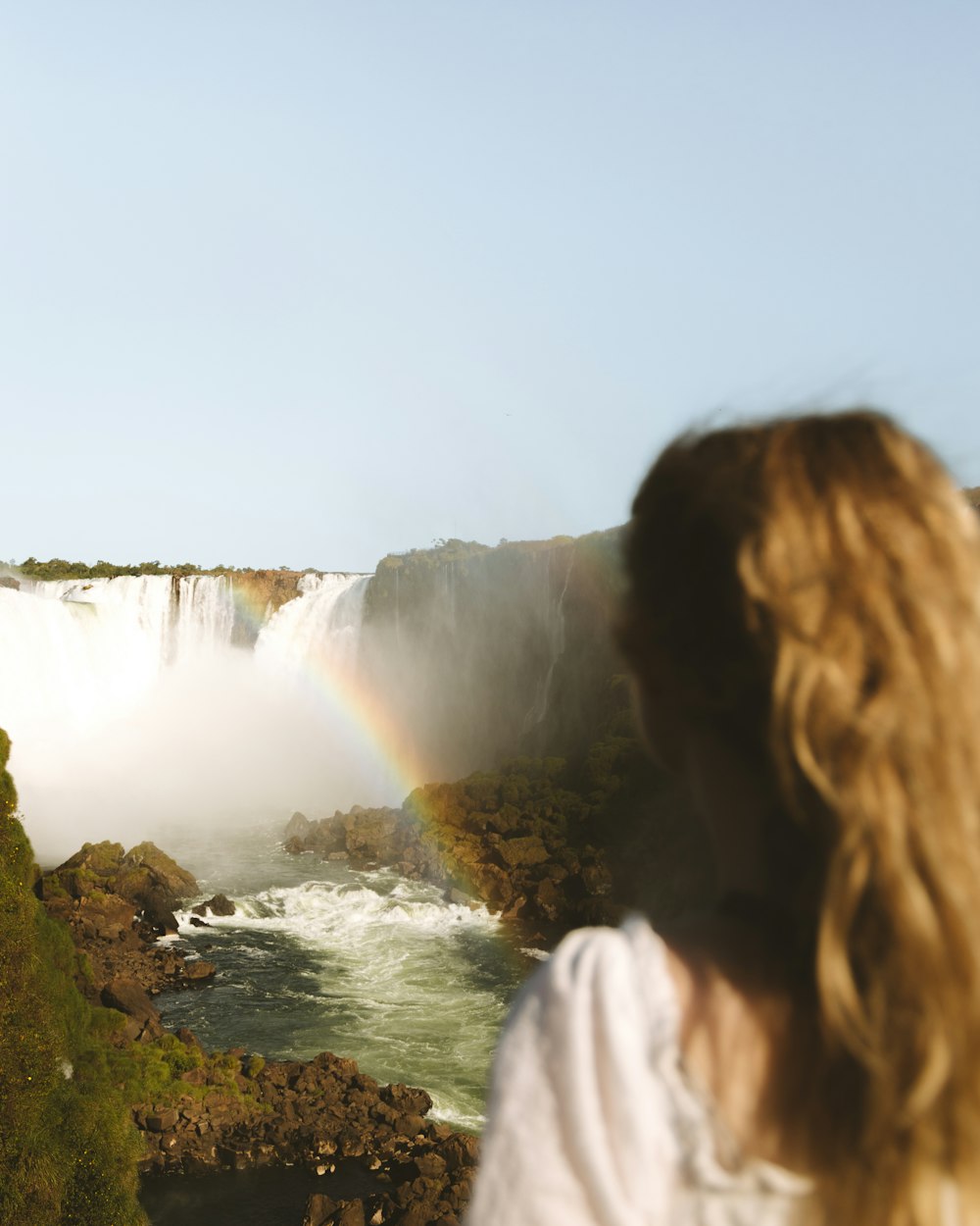 woman in white shirt standing on green grass near waterfalls during daytime
