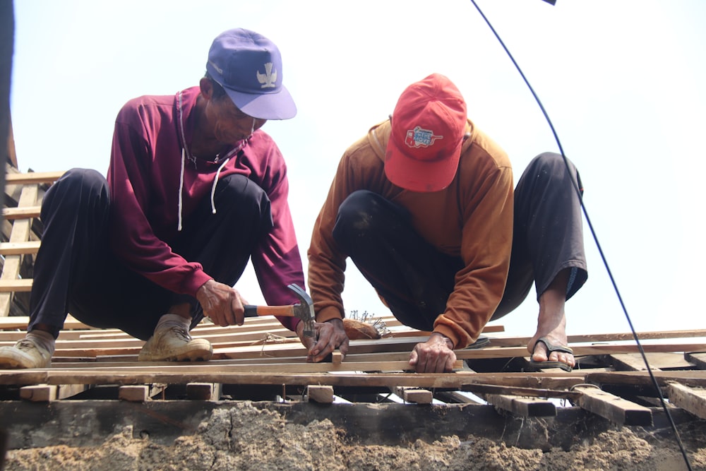 2 men in red knit cap and black long sleeve shirt sitting on brown wooden dock