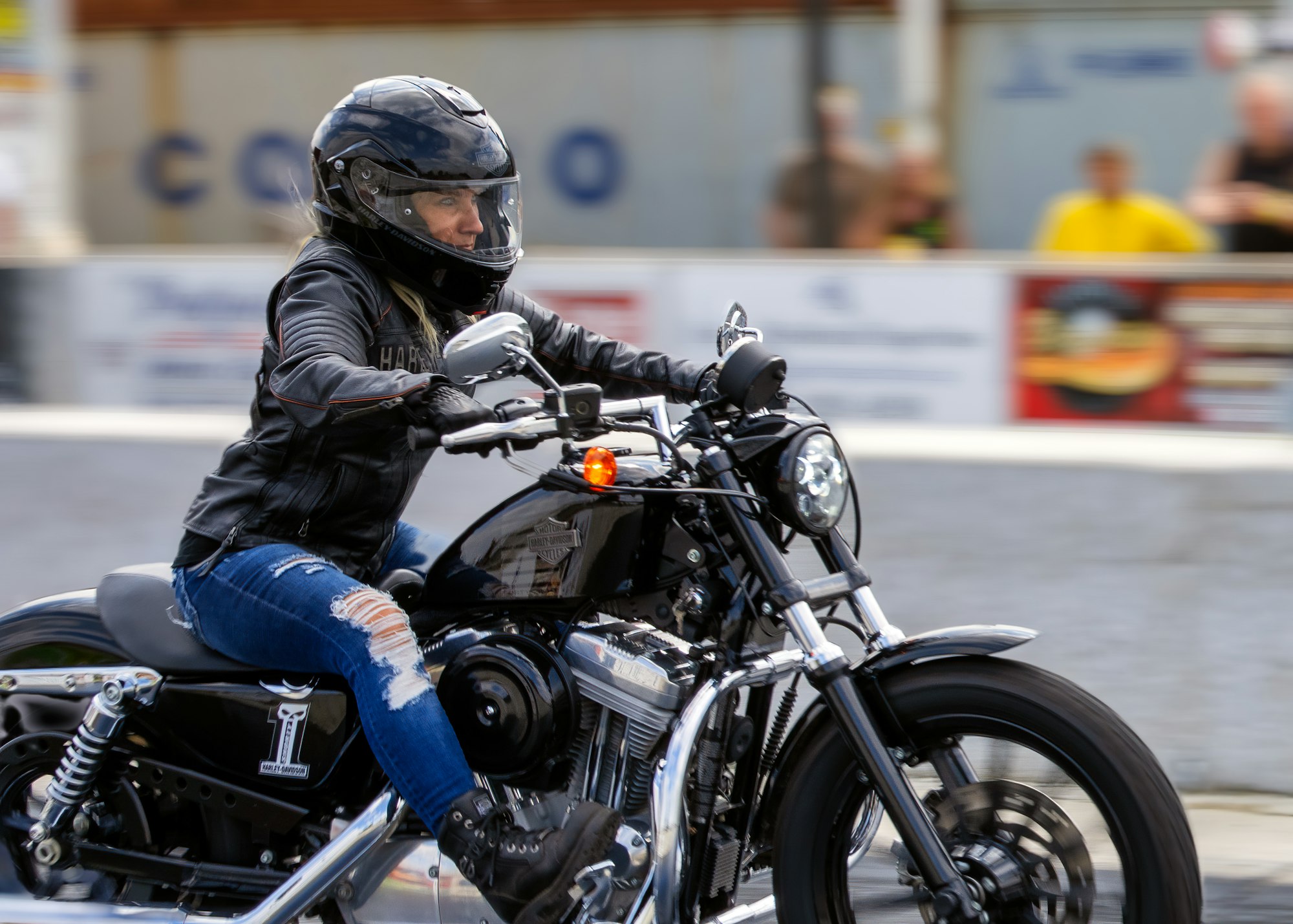 Woman riding motorcycle wearing helmet and ripped jeans.
