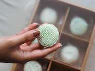 Hands wrapping a beautifully boxed assortment of pastries tied with a green pistachio-colored ribbon.