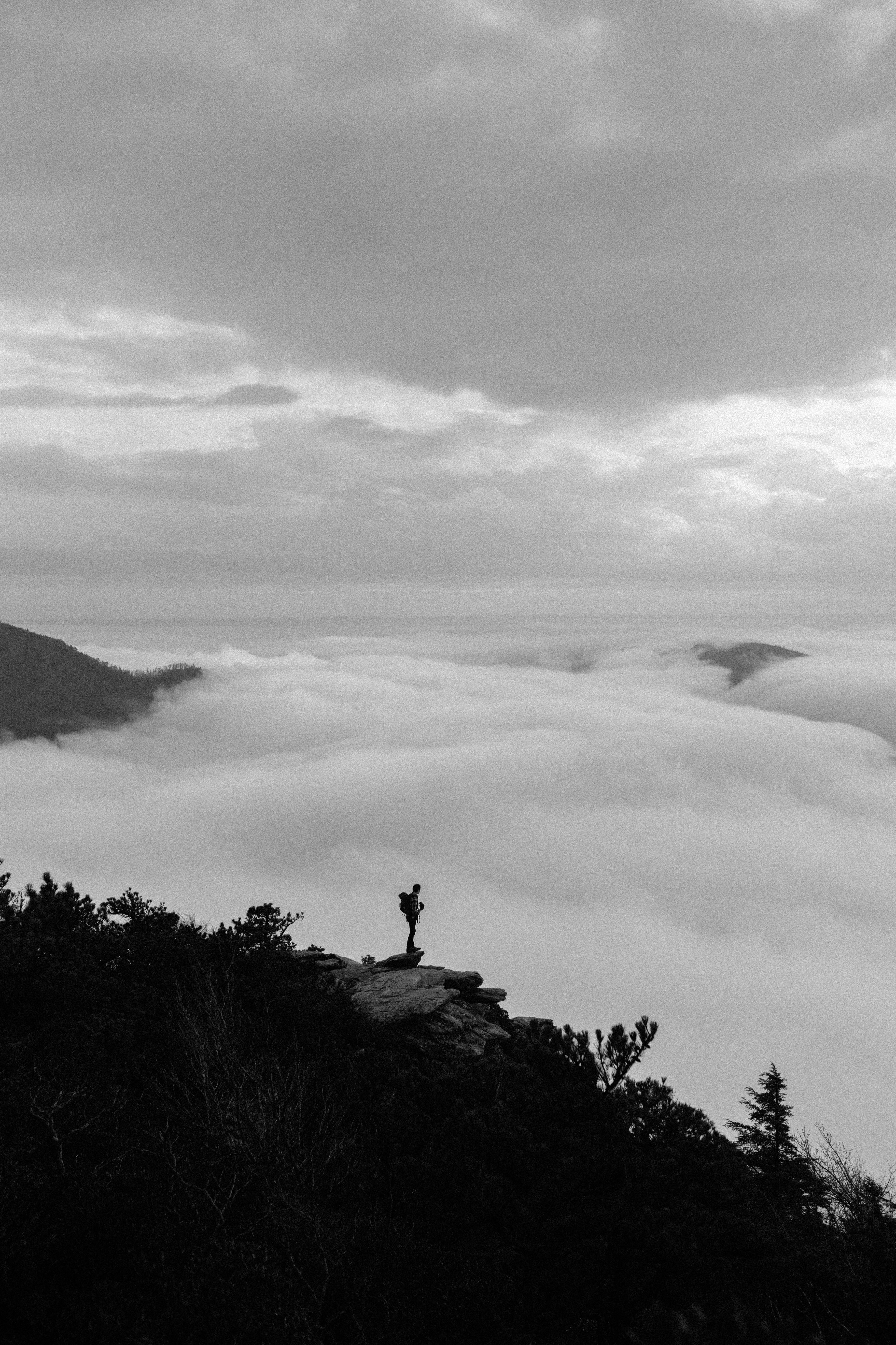 foto em tons de cinza da pessoa sentada na rocha perto da montanha