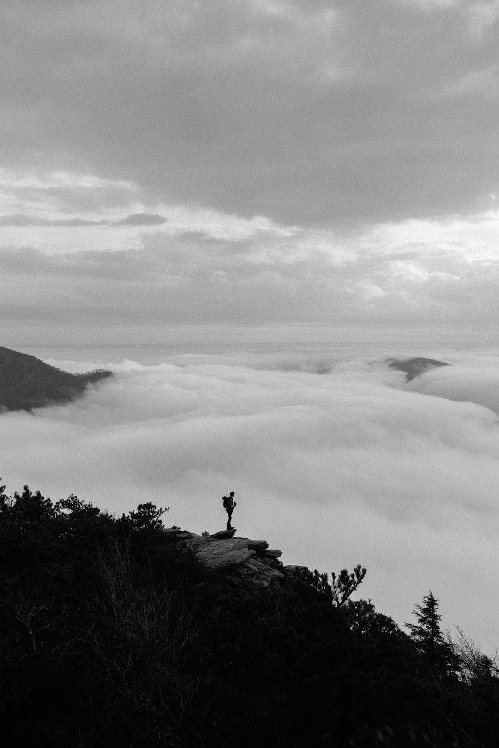 Graustufenfoto einer Person, die auf einem Felsen in der Nähe eines Berges sitzt