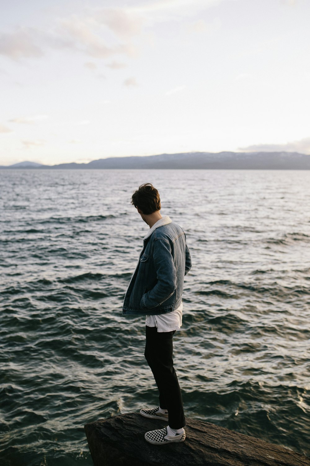 man in white dress shirt and black pants standing on sea shore during daytime