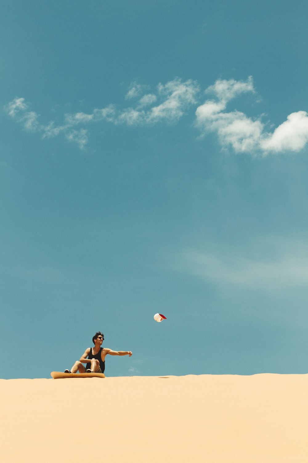 man in black shorts sitting on brown sand under blue sky during daytime