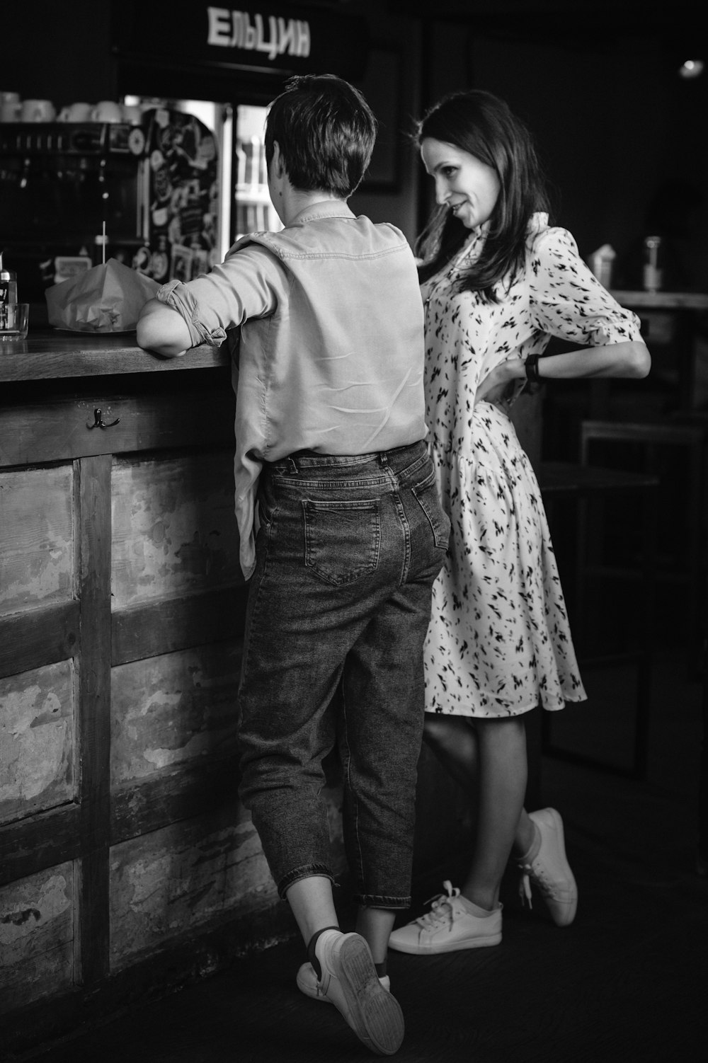 grayscale photo of man and woman standing beside wooden table