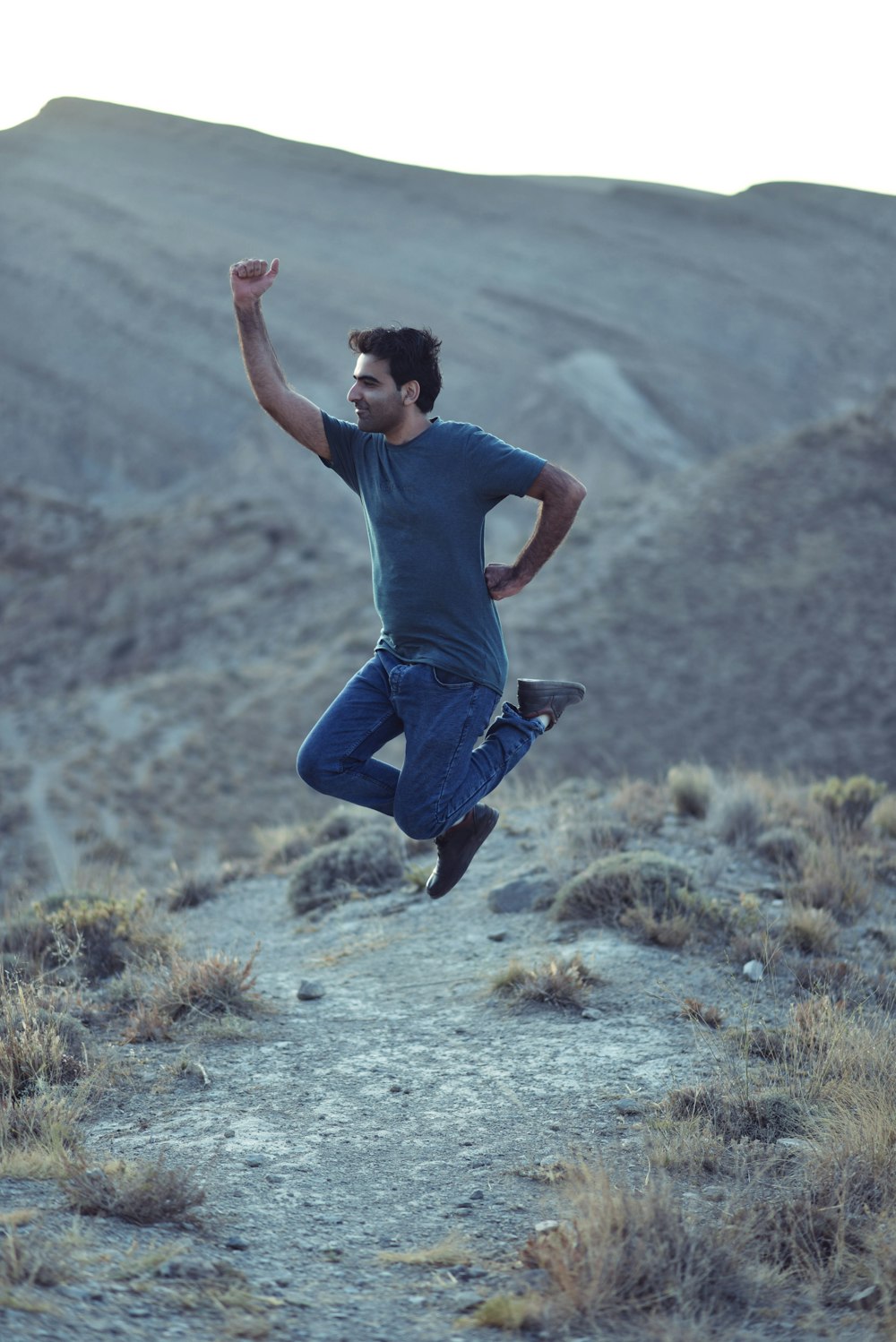 man in blue crew neck t-shirt and blue denim jeans jumping on gray dirt road