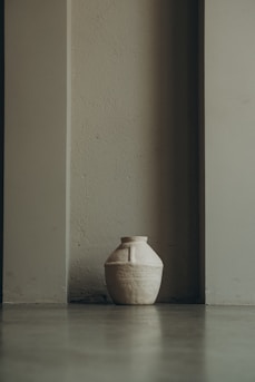 A rustic ceramic vase with a matte finish sitting on a wooden table bathed in soft natural light.