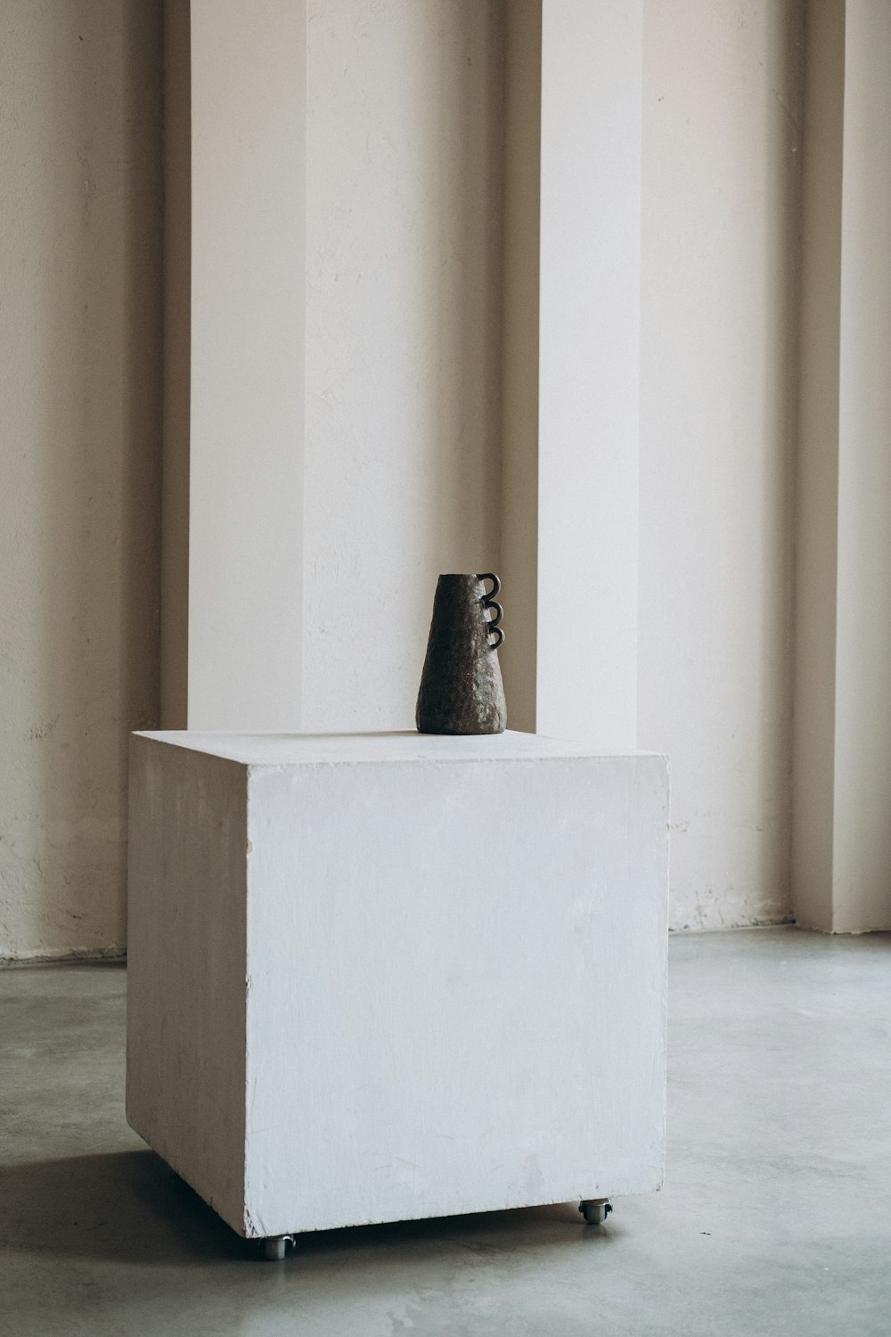 白いコンクリートの壁に黒い陶器の花瓶