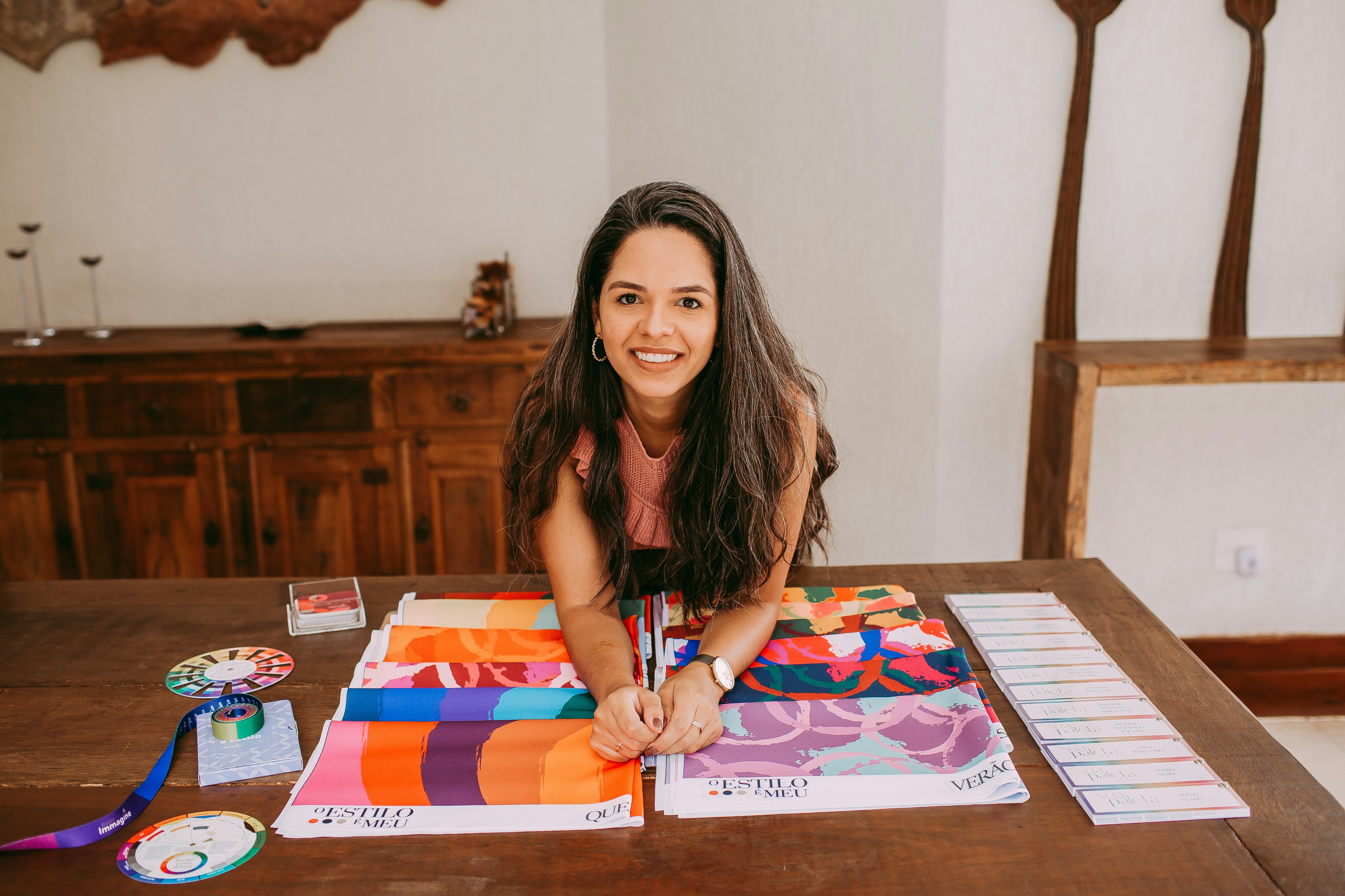Professional headshot of a woman interior designer, warm smile, bright studio environment, fabric swatches and material samples visible