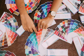 Hands arranging color swatches in muted browns and greenish-grays on a clean desk.
