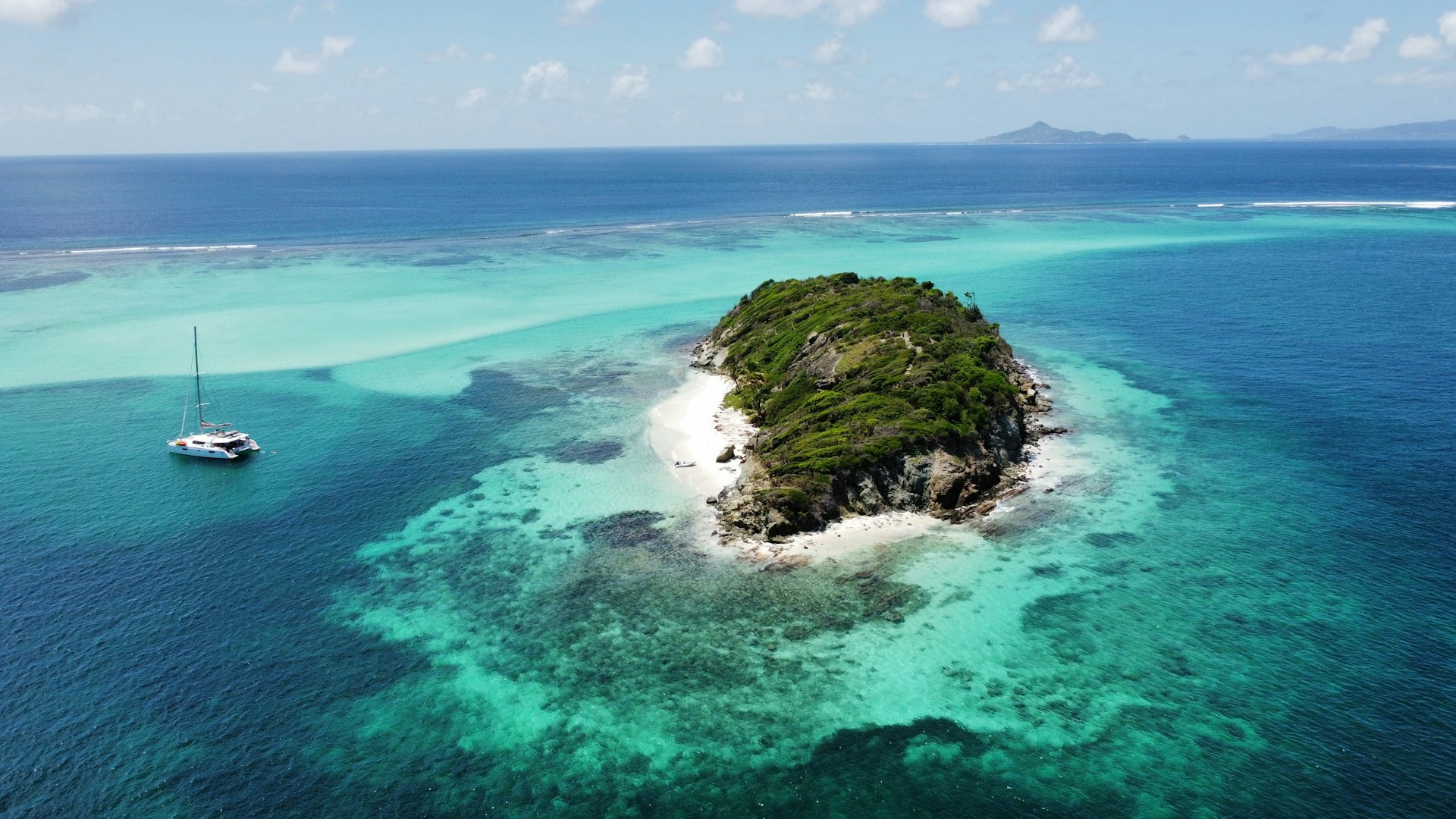 A sunlit view of the Tooth Ferry catamaran anchored near the crystal-clear waters of Virgin Gorda, with the lush island landscape in the background.