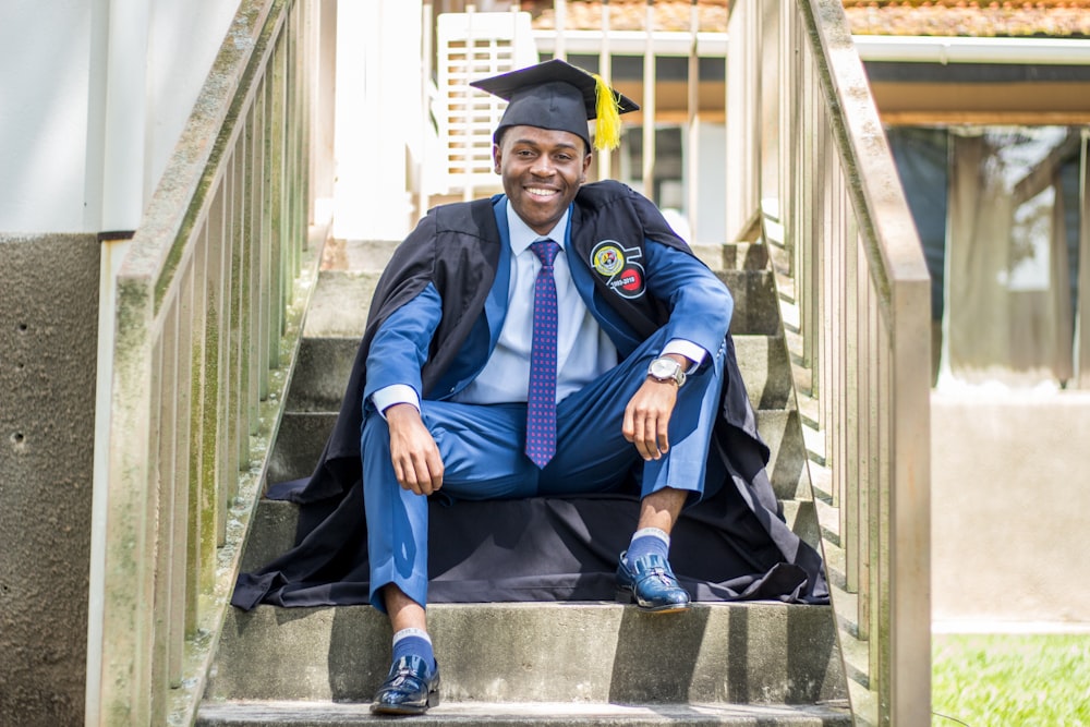 a man in a graduation cap and gown sitting on steps