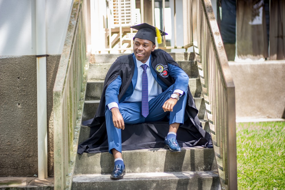 階段に座っている卒業式の帽子とガウンを着た男