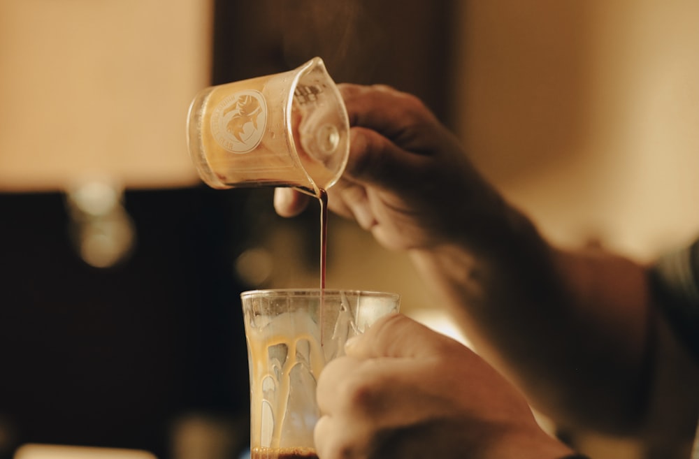 person holding clear drinking glass with brown liquid