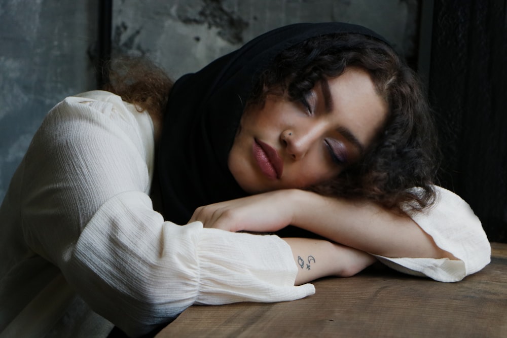 woman in white long sleeve shirt leaning on brown wooden table