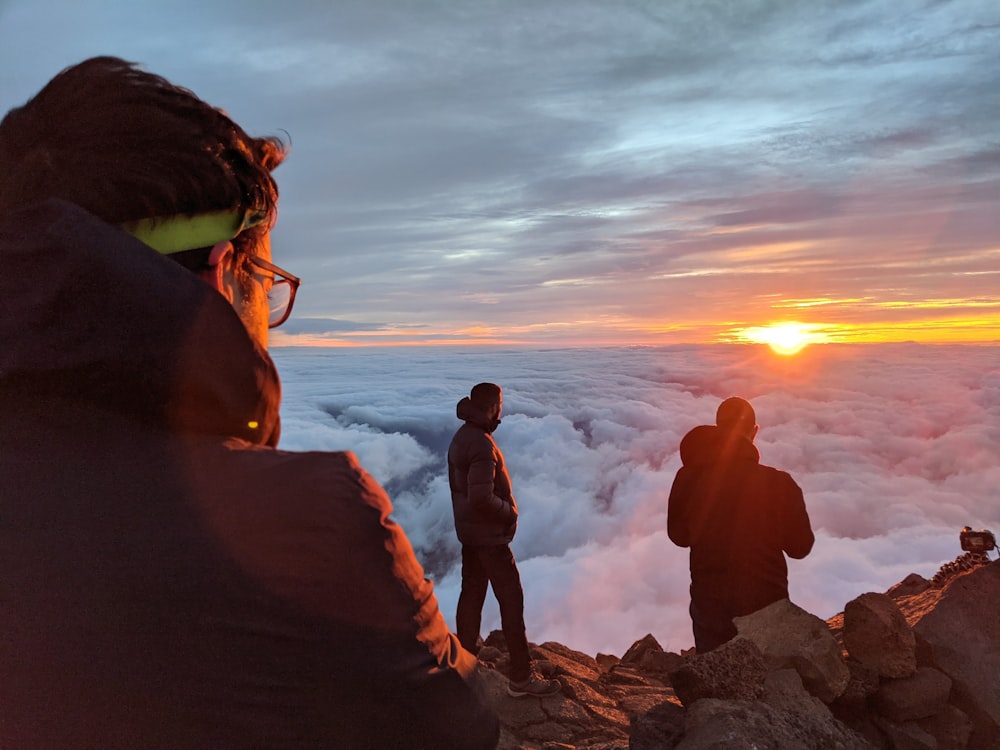 silhouette of 3 men standing on rock formation near body of water during sunset