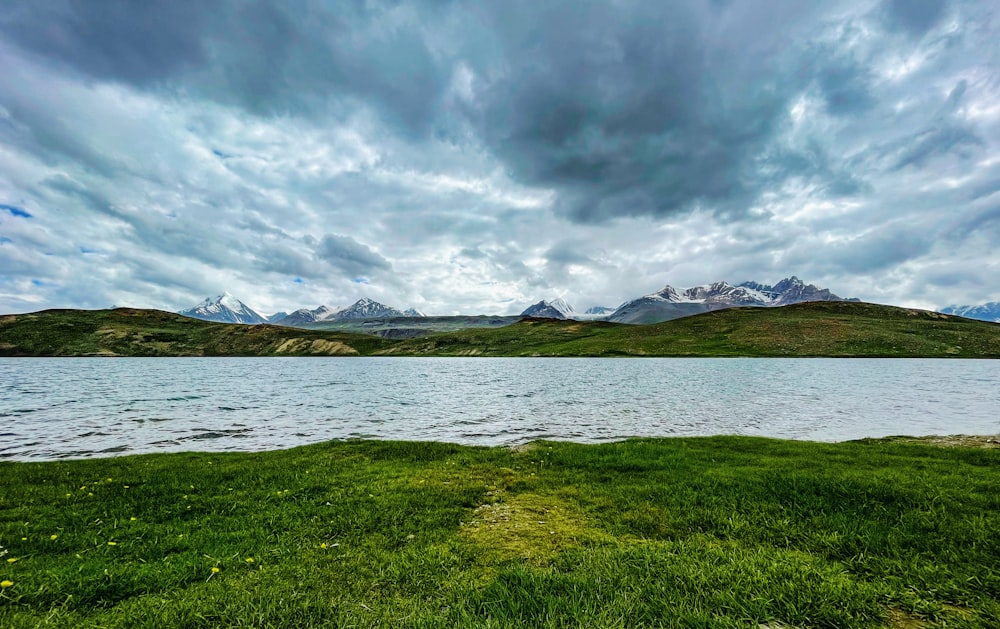 green grass field near body of water under cloudy sky during daytime