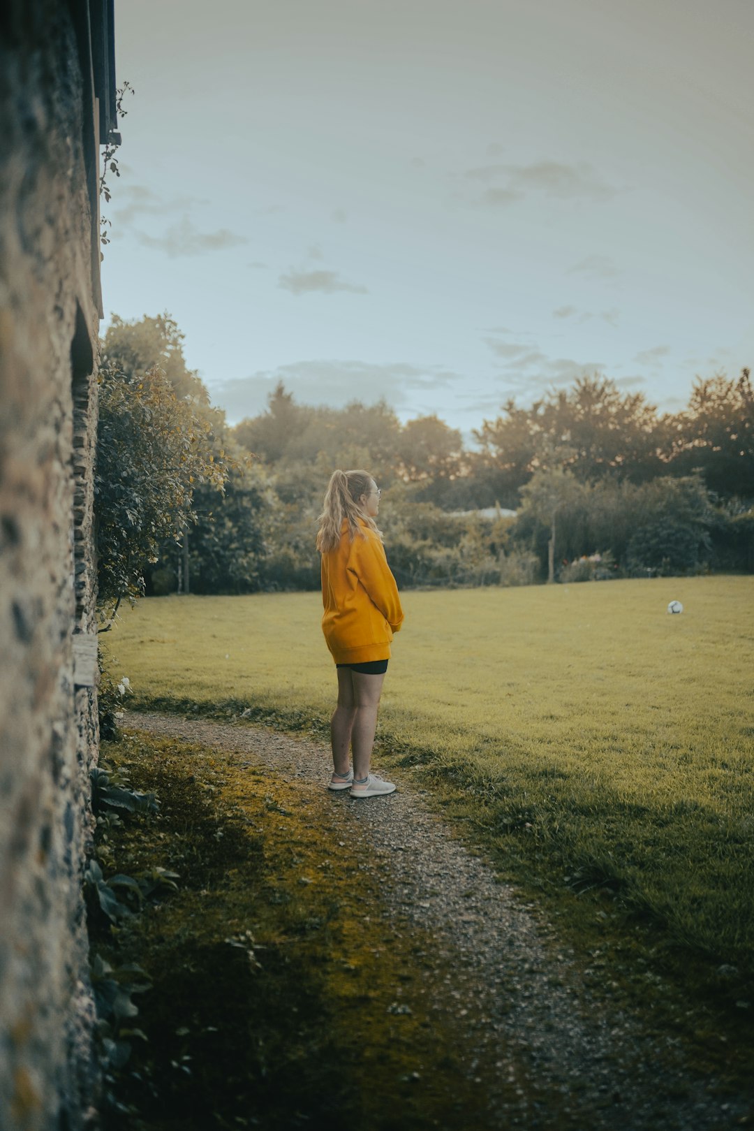 woman in orange long sleeve shirt and white shorts standing on green grass field during daytime