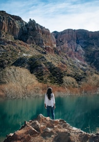 woman in white dress standing on brown rock formation near lake during daytime