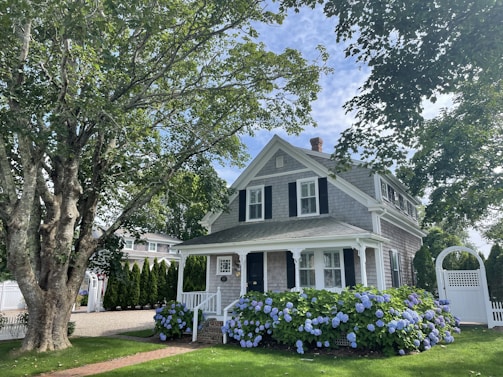 white and gray wooden house near green trees under white clouds during daytime