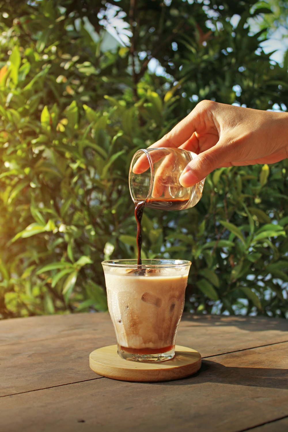 person pouring brown liquid on clear drinking glass