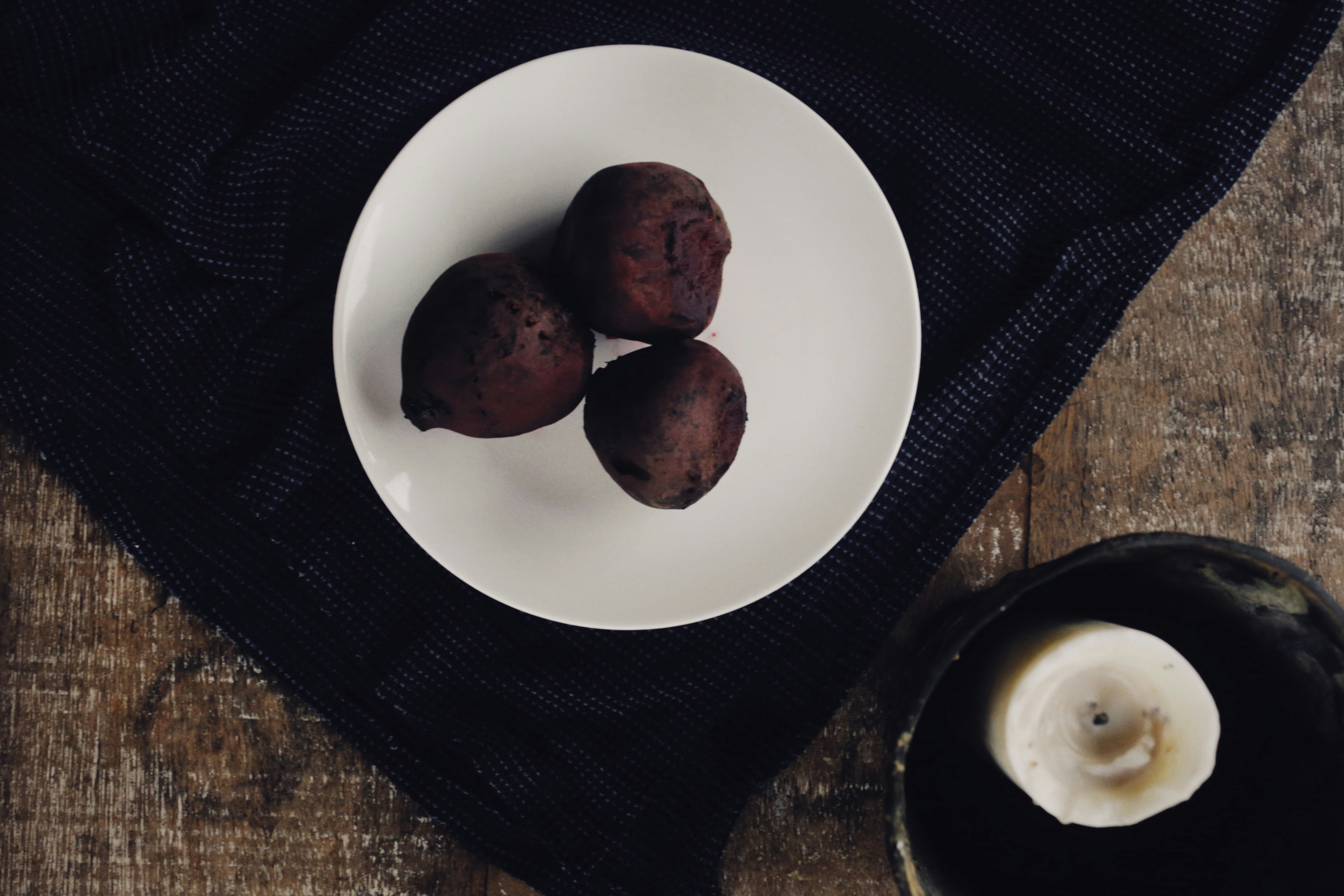 Artistic plating of roasted beet dish on dark ceramic plate, deep crimson and earth tones, candlelight from left side, dark moody background