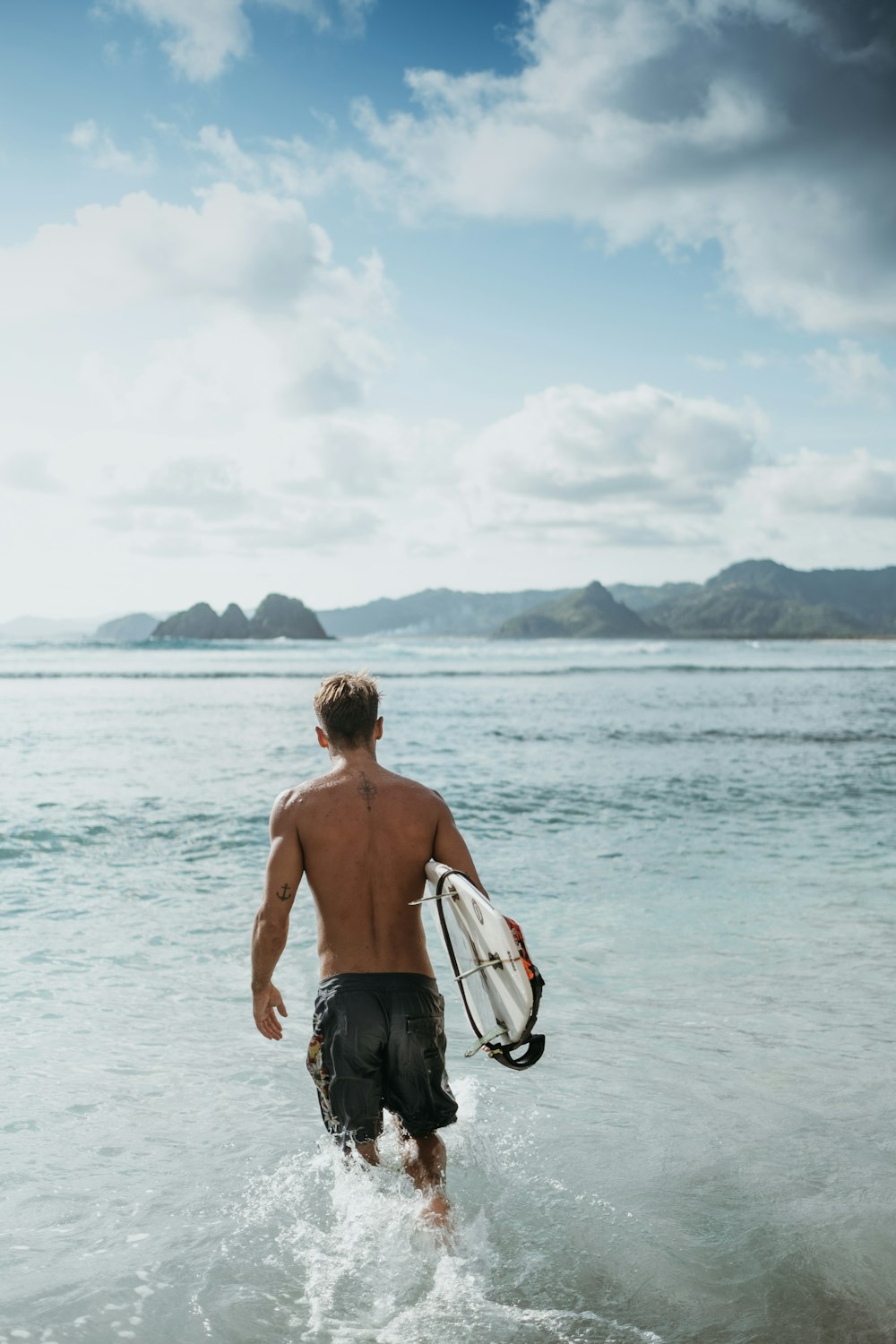 topless man in black shorts holding white and black surfboard on sea during daytime