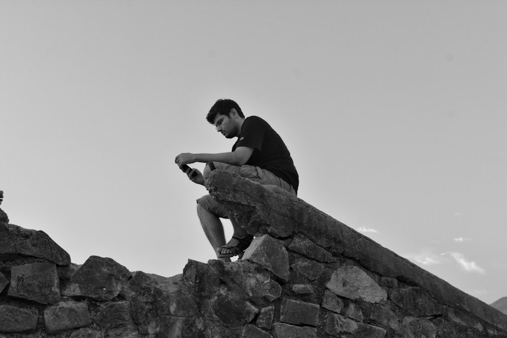 man in black shirt sitting on rock