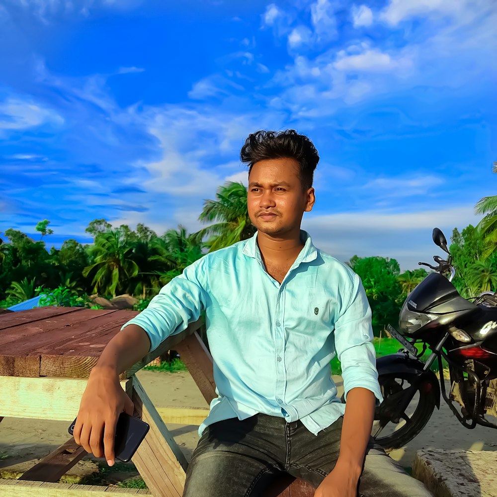 man in green dress shirt sitting on brown wooden bench during daytime