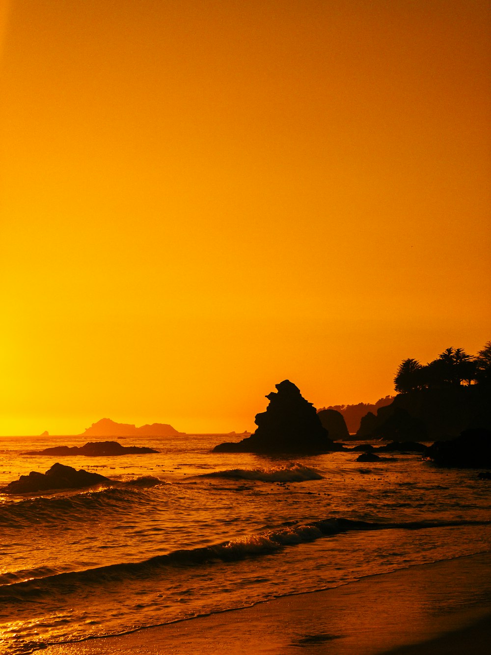 silhouette of rock formation on sea during sunset