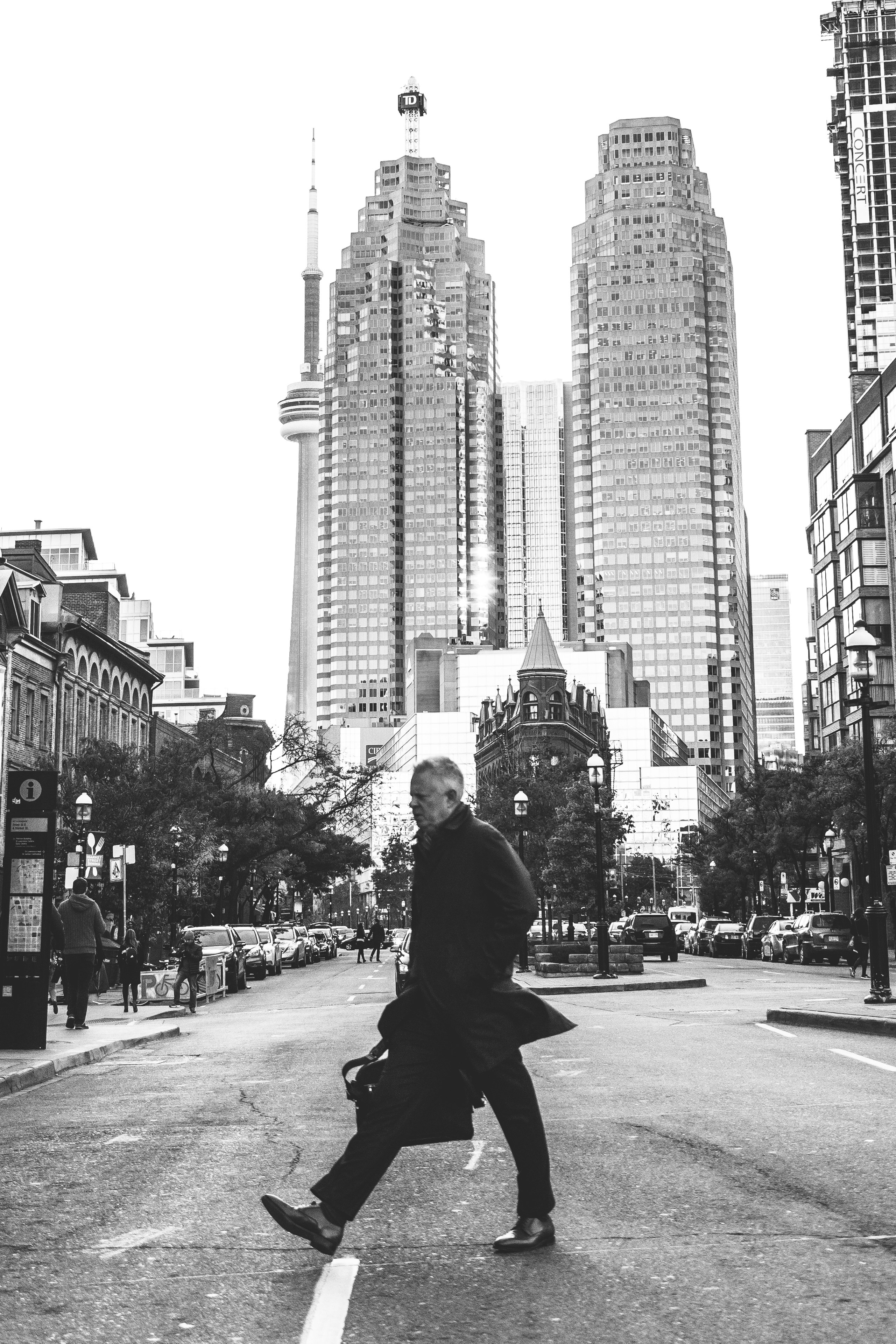 grayscale photo of man sitting on sidewalk near city buildings