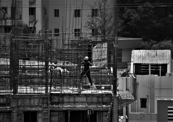 grayscale photo of man in black jacket and pants standing on building