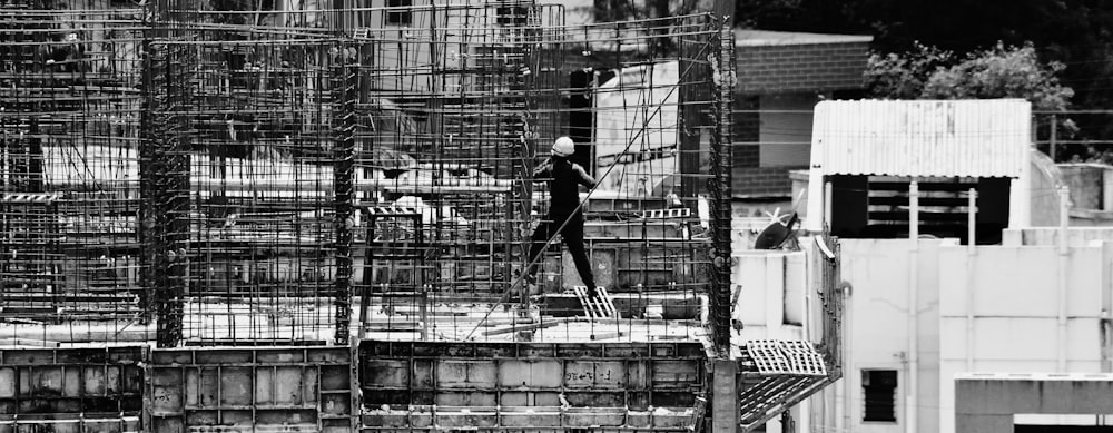 grayscale photo of man in black jacket and pants standing on a ladder