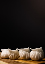 Several neatly arranged white dumplings rest on a wooden surface against a dark background. Their pleated shapes give them an appealing, handcrafted appearance.