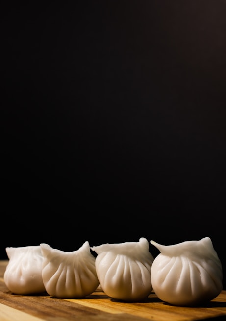 Several neatly arranged white dumplings rest on a wooden surface against a dark background. Their pleated shapes give them an appealing, handcrafted appearance.
