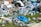 Scattered garbage including plastic bottles, plastic bags, cans, and cardboard boxes are strewn across green grass. The trash is a mix of different materials and colors, indicating improper waste disposal.