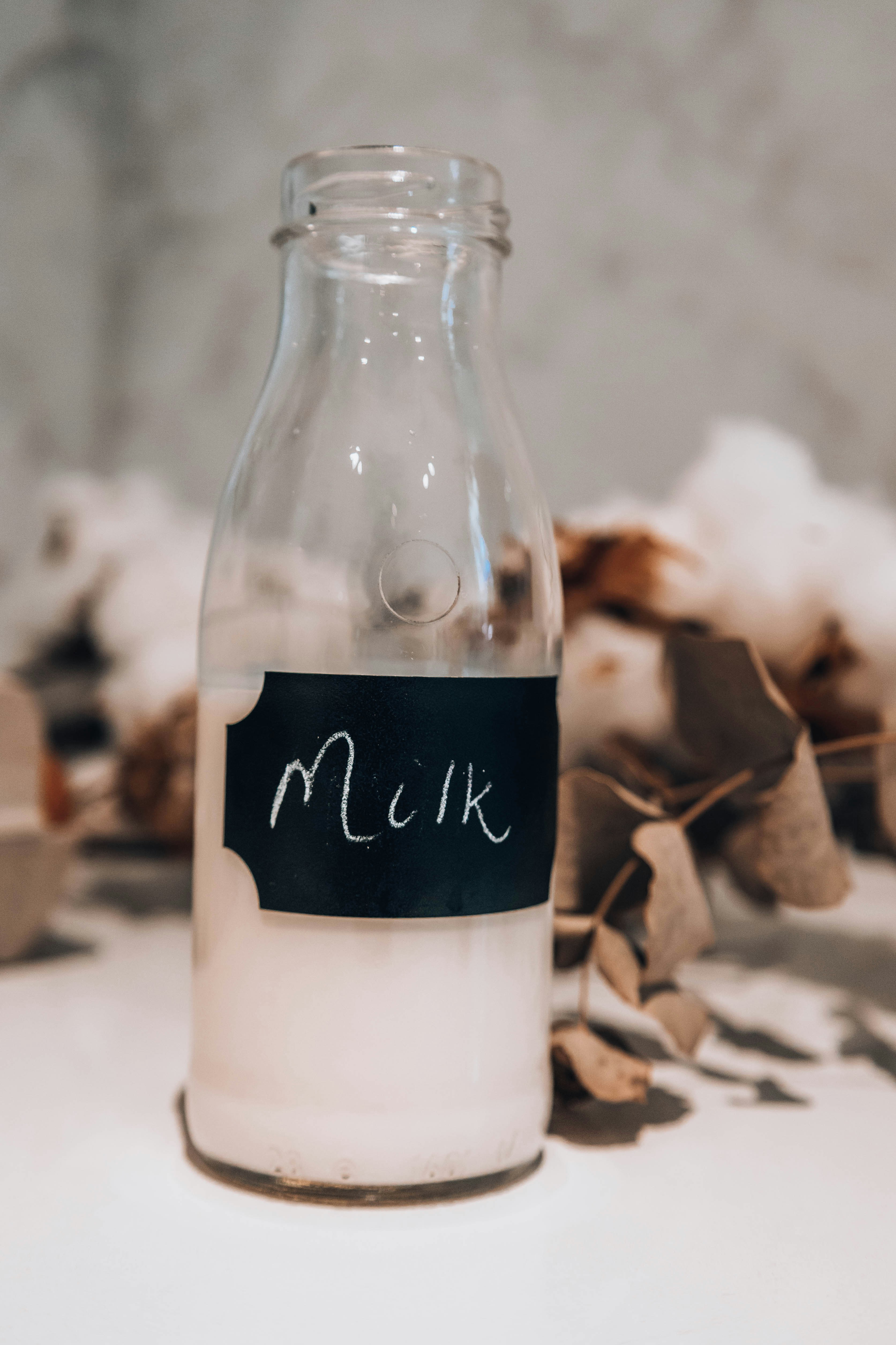 White glass bottle of whole milk on clean white surface
