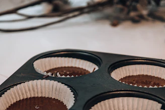 Close-up of golden baking molds filled with rich chocolate batter on a warm beige background