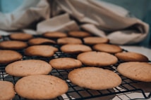 A batch of freshly baked cookies cooling on a metal wire rack, with a soft and warm appearance. The background features a cozy fabric and soft lighting, enhancing the homey atmosphere.