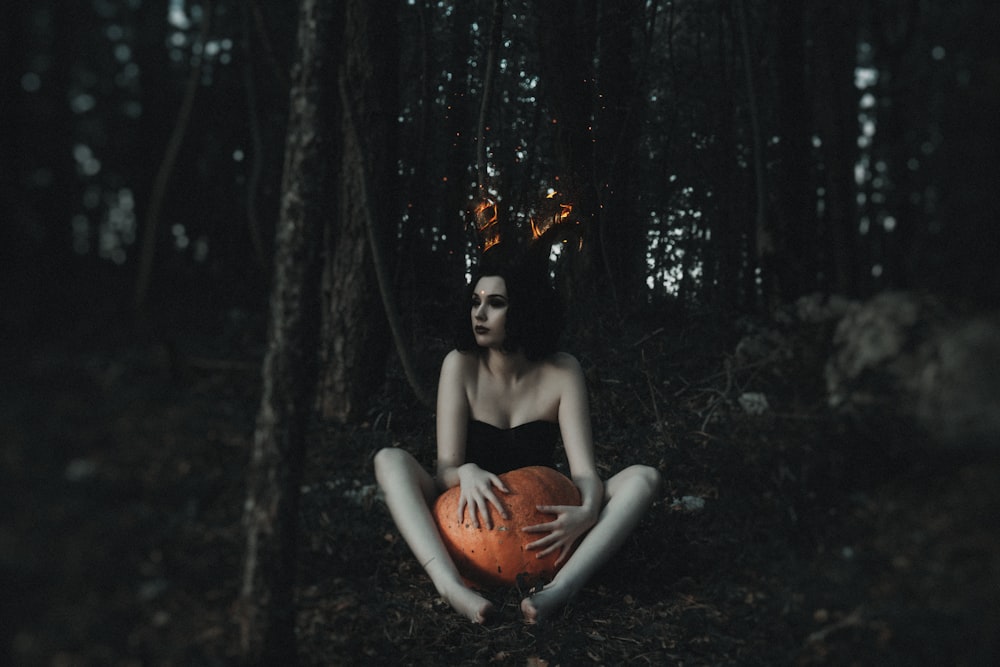 woman in orange dress sitting on brown rock in the middle of forest during daytime