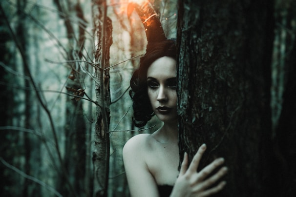 A scene showcasing a model wearing shadowy makeup and a tattered cloak, standing in a fog-draped forest.
