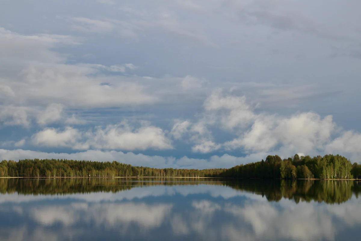 Forest and white clouds mirrored in a still lake near Mora