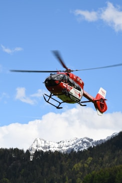 red and black helicopter flying over snow covered mountain during daytime